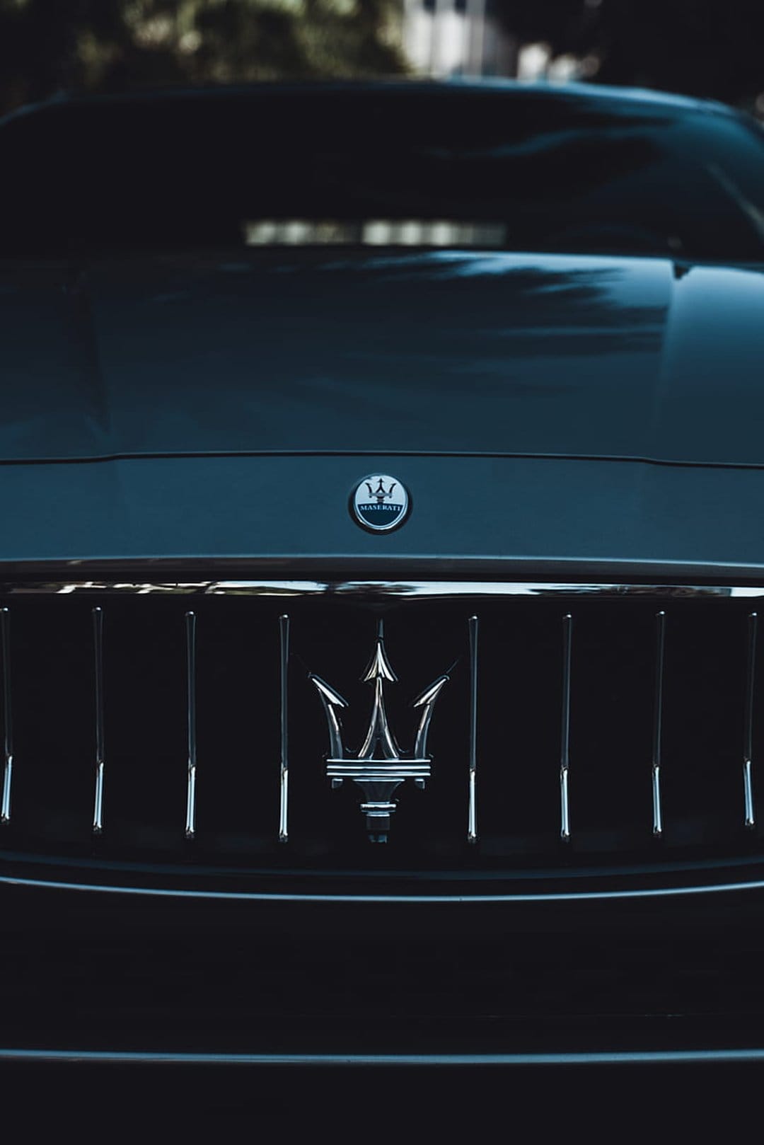 Polished Maserati trident logo sits against a black mesh car grille, highlighting luxury automotive details.