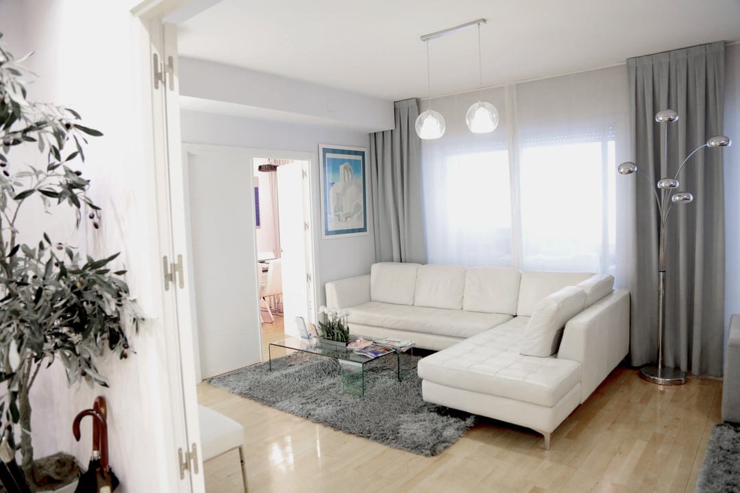 White sectional sofa on a gray shag rug next to a glass coffee table in a bright, modern minimalist living room.