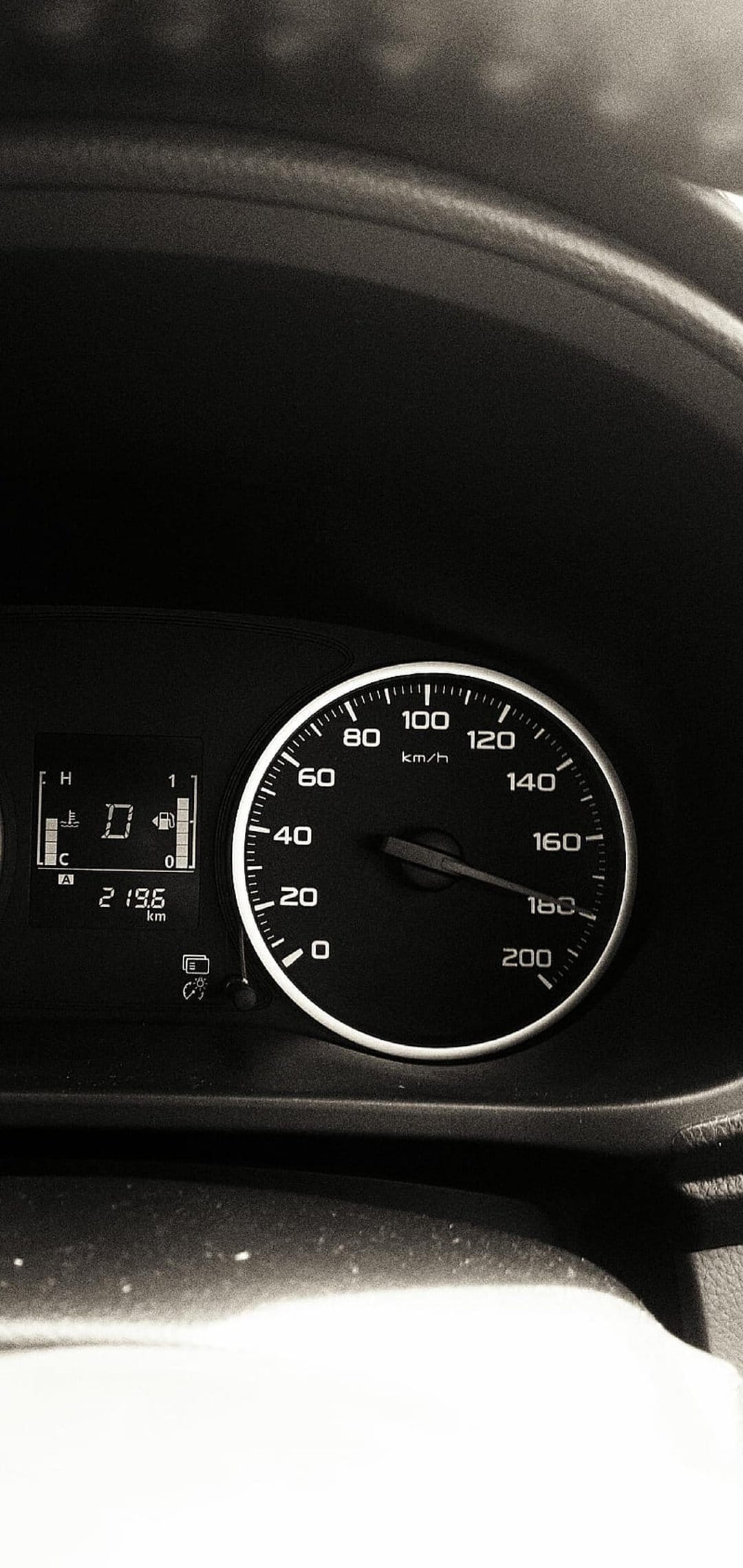 Black analog speedometer needle pointing at 120 km/h beside a digital display showing gear and fuel info.