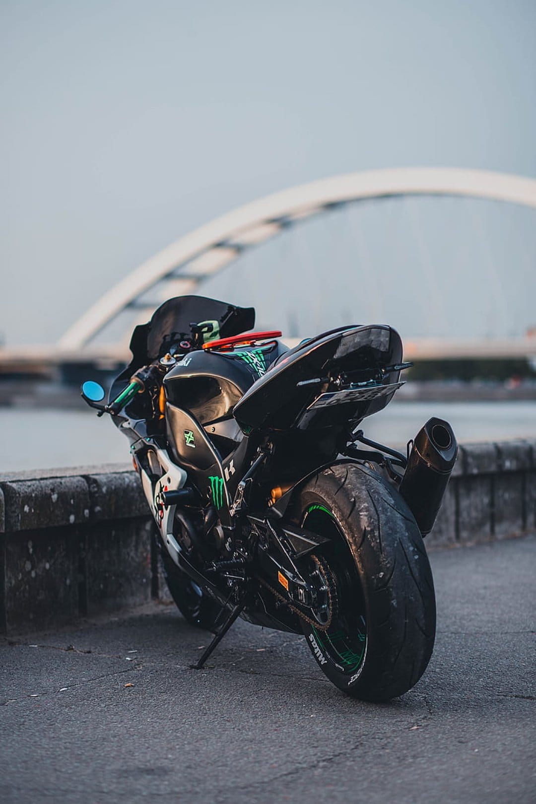 Black Kawasaki motorcycle with green accents parked near a white arched bridge during a hazy sunset.