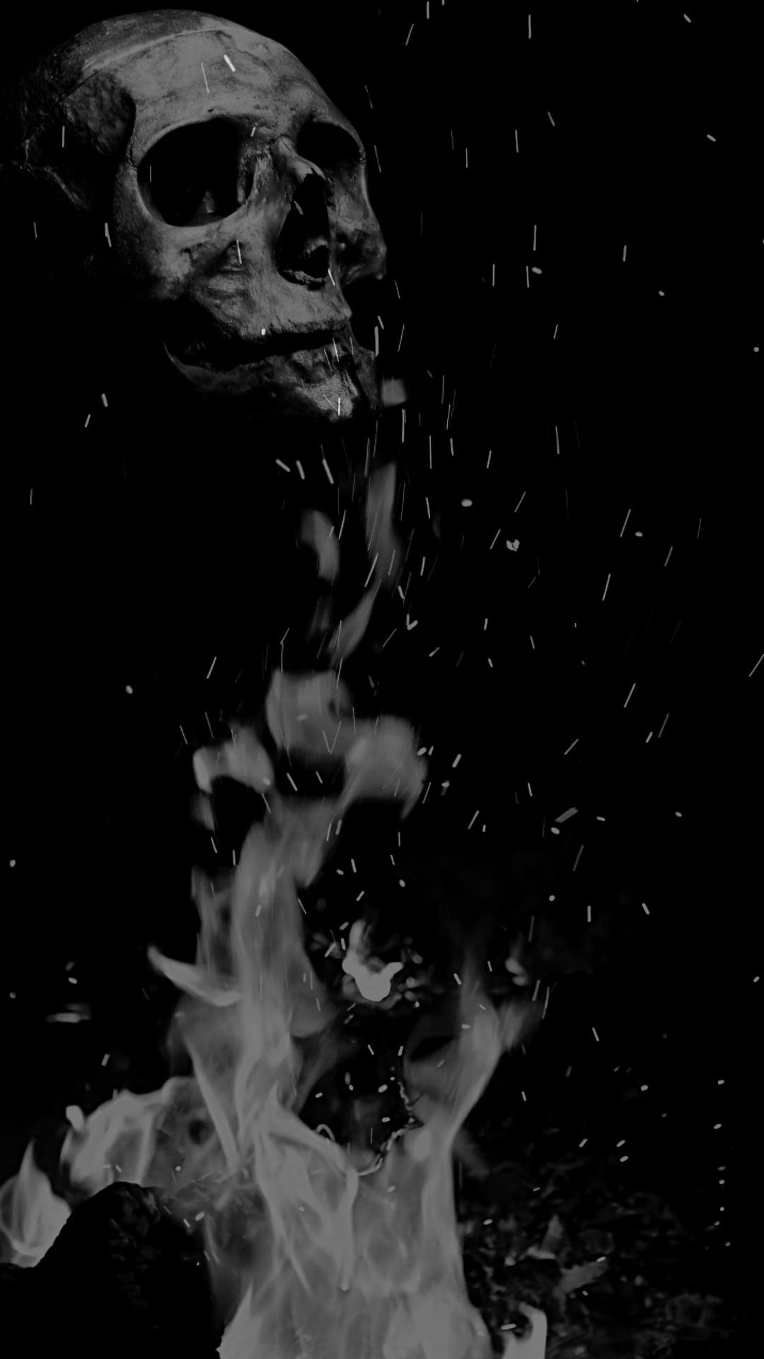 Human skull positioned above rising flames and scattered sparks against a dark monochrome background.