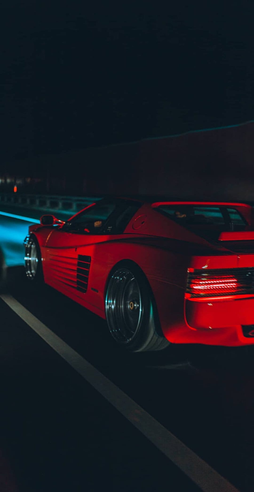 Red Ferrari Testarossa speeds through a dark tunnel with glowing red taillights and blue light reflections.
