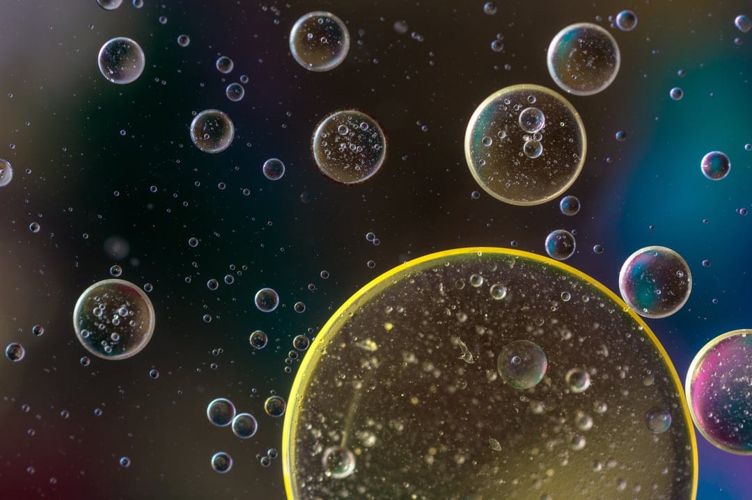 Iridescent oil bubbles with prismatic reflections float over a dark background in a detailed macro composition.