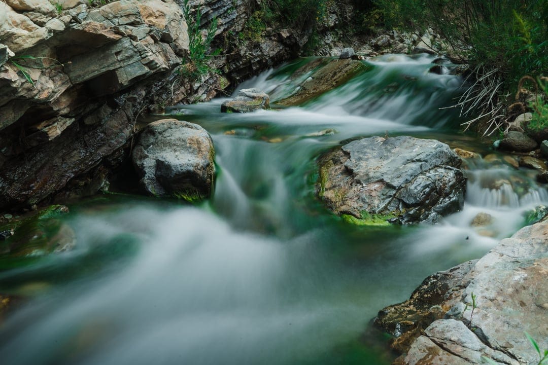 Emerald river water cascading over smooth grey stones in a deep rocky canyon with a silky motion blur effect.