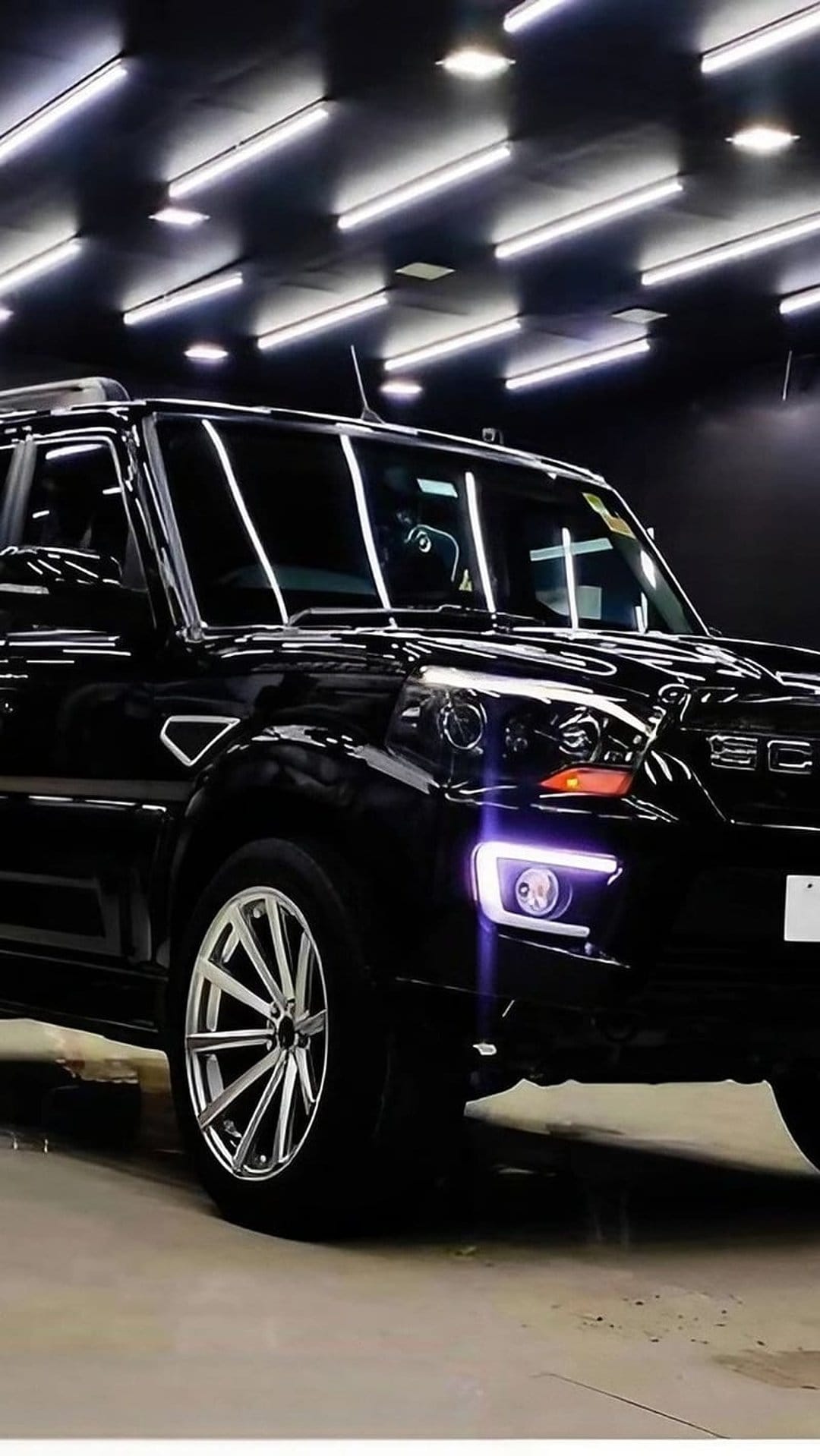 Mahindra Scorpio-N SUV in black sits in a dark studio with glowing LED headlights and custom alloy wheels.