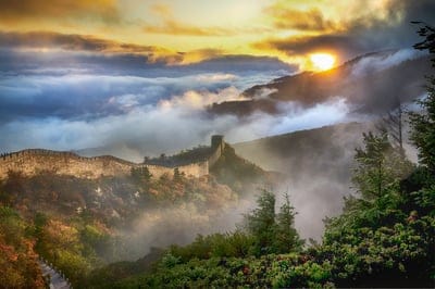 Great Wall of China watchtowers emerge from thick morning fog under a golden sunrise in a vertical landscape.