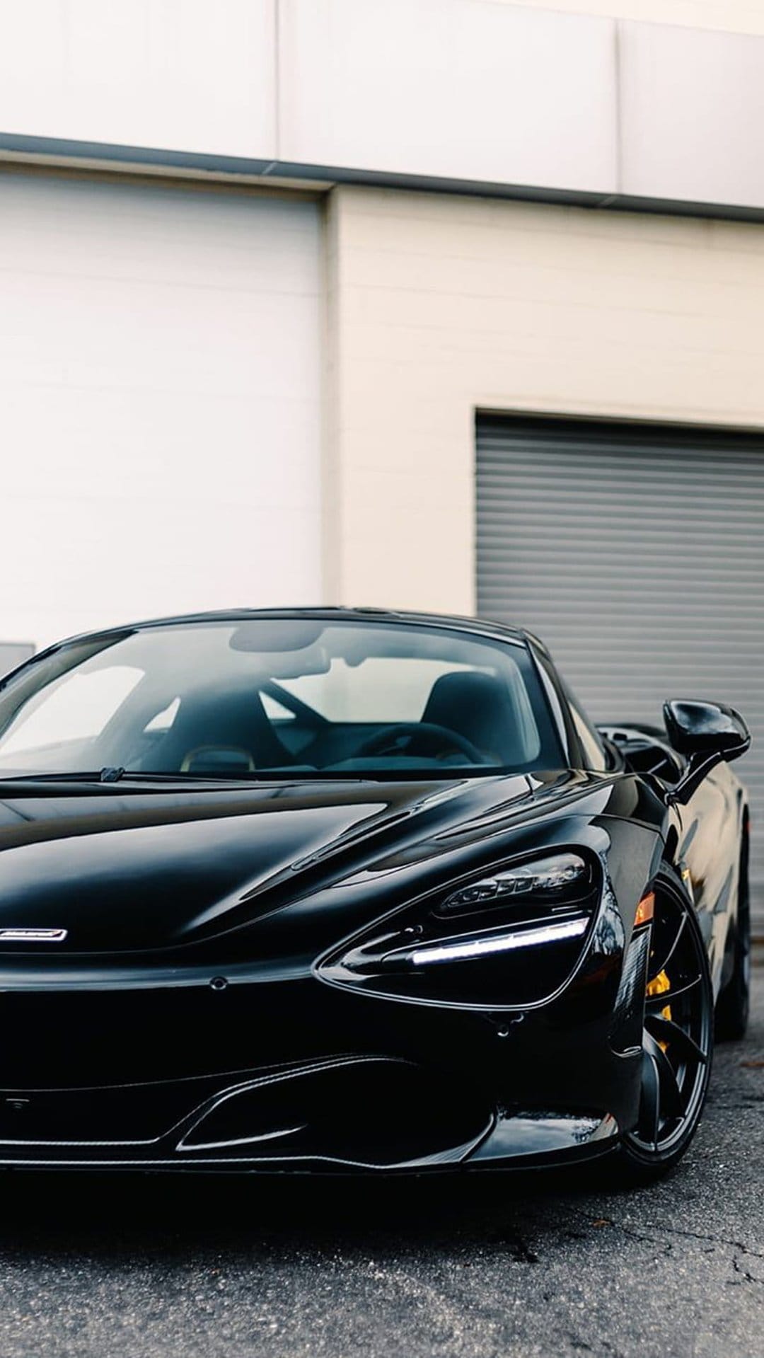 McLaren 720S supercar in glossy black features yellow brake calipers and sharp LED headlights at a low angle.