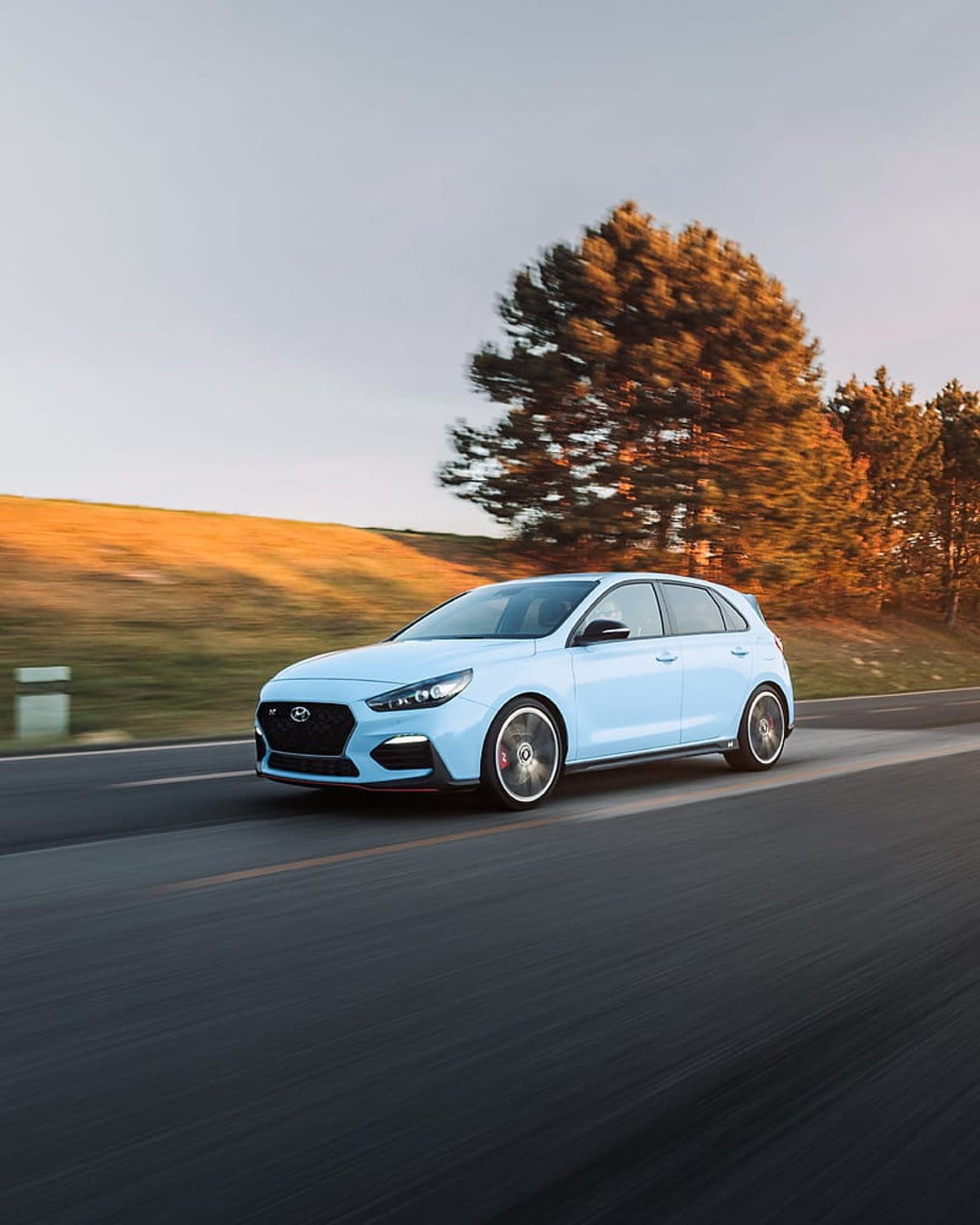 Hyundai i30 N hatchback driving on a scenic road with golden hour lighting and hills in the background.