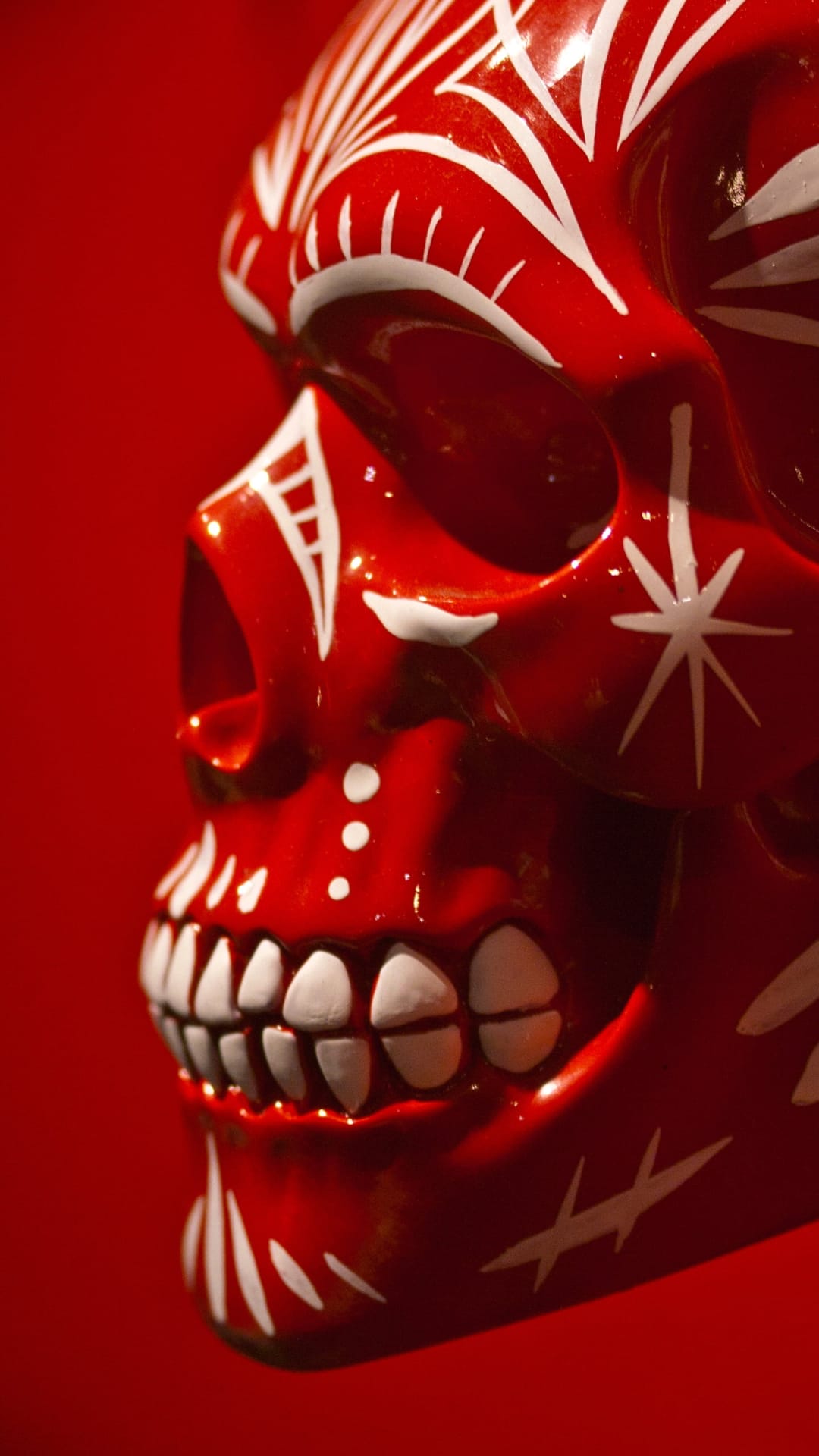 Red skull with white floral patterns and ornate filigree carvings centered on a solid crimson background.