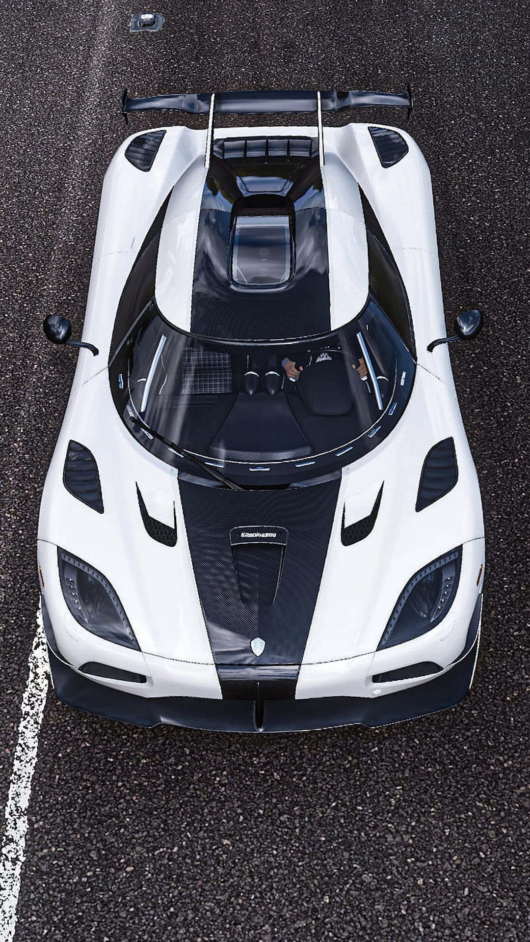 White Koenigsegg supercar with black stripes seen from directly above on a dark asphalt racetrack surface.