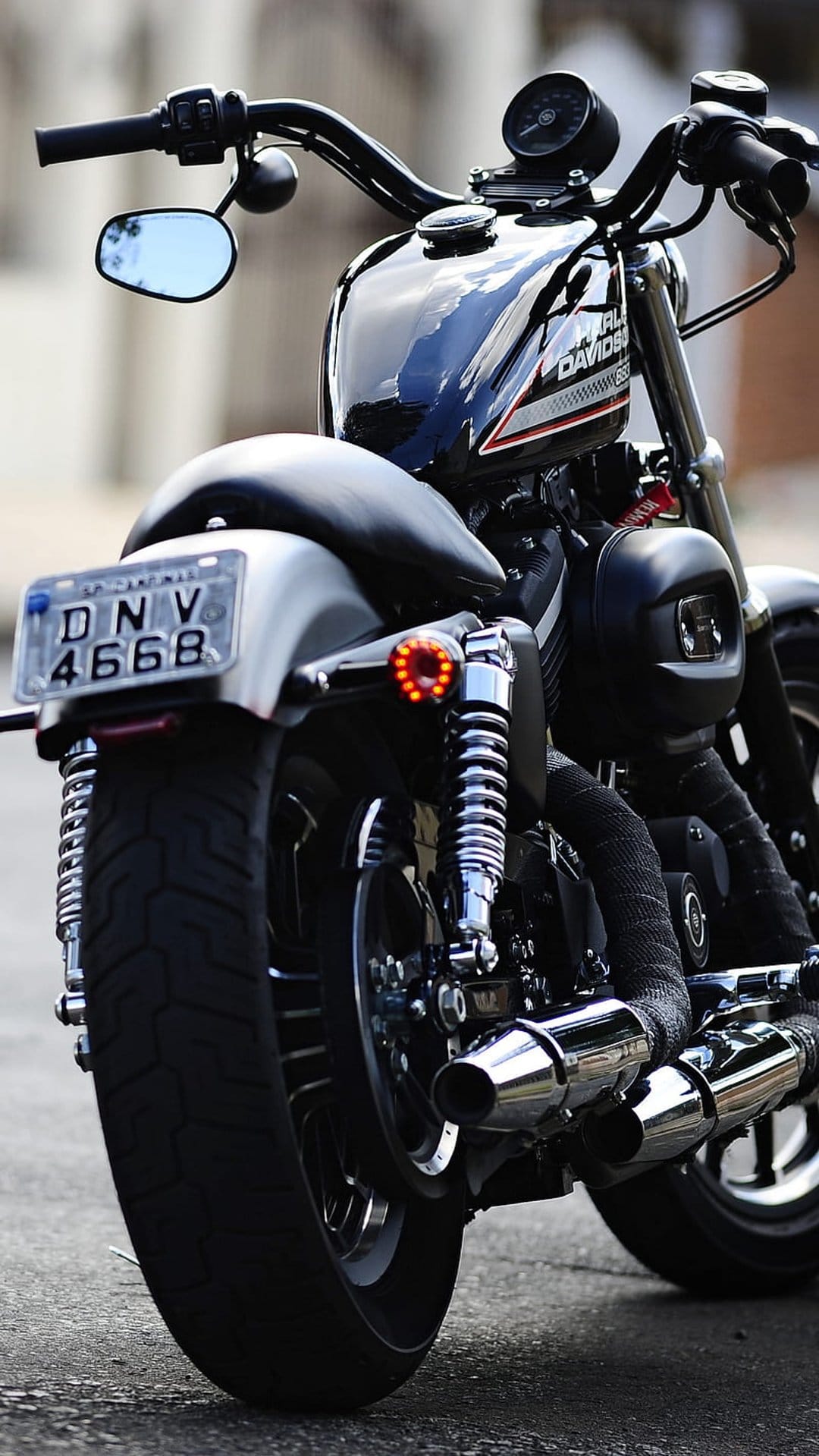 Chrome motorcycle exhaust pipes and a red taillight highlight the rear view of a black cruiser motorbike.