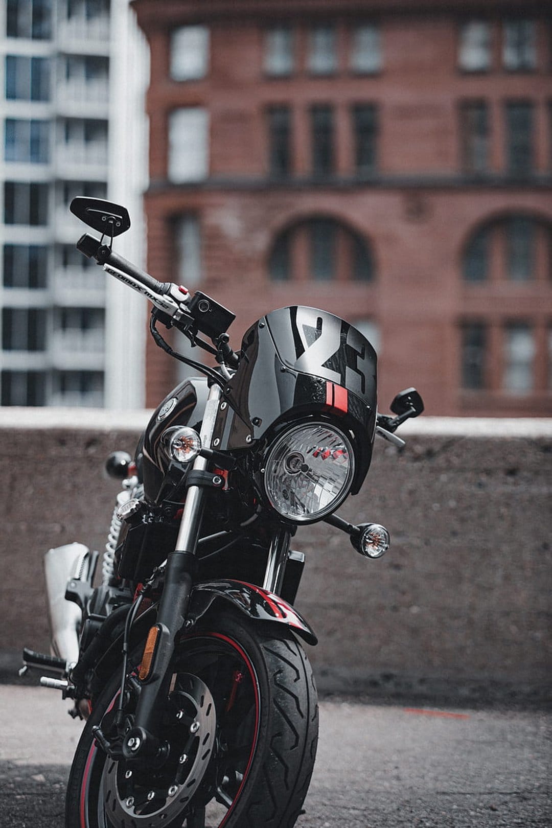 Black sportbike with a number 2 decal and red stripes parked on a city street with a blurred urban background.