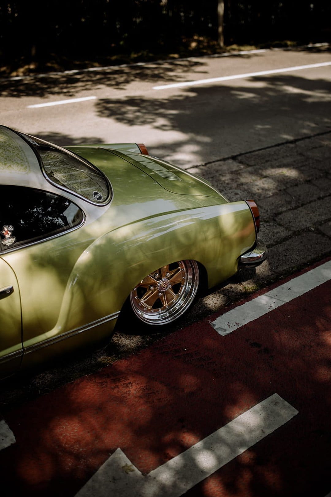 Mint green vintage car rear with polished chrome wheels parked on a sun-dappled street with red markings.