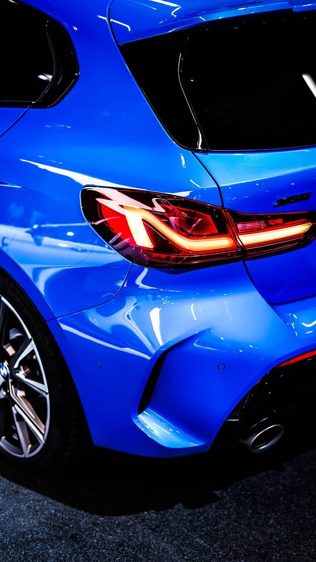 Blue BMW rear bumper and glowing red LED taillights featuring sharp body lines and a metallic paint finish.