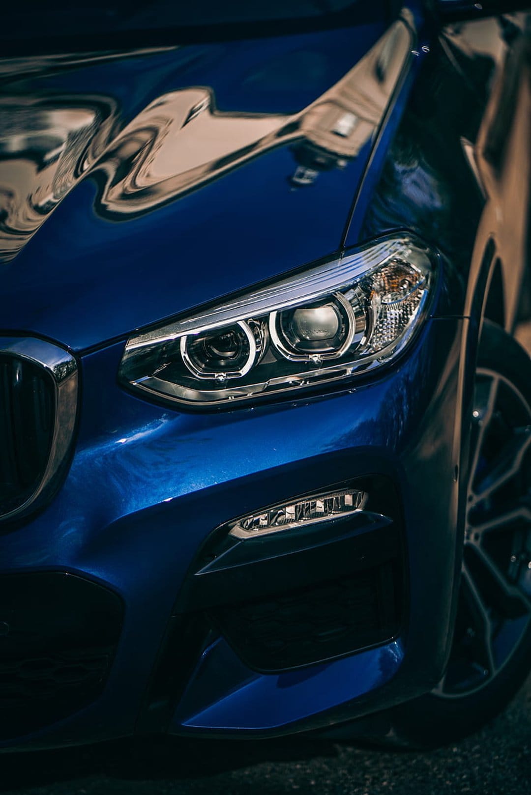 Blue BMW SUV front headlight and chrome grille showing intricate LED structures and a polished metallic exterior.