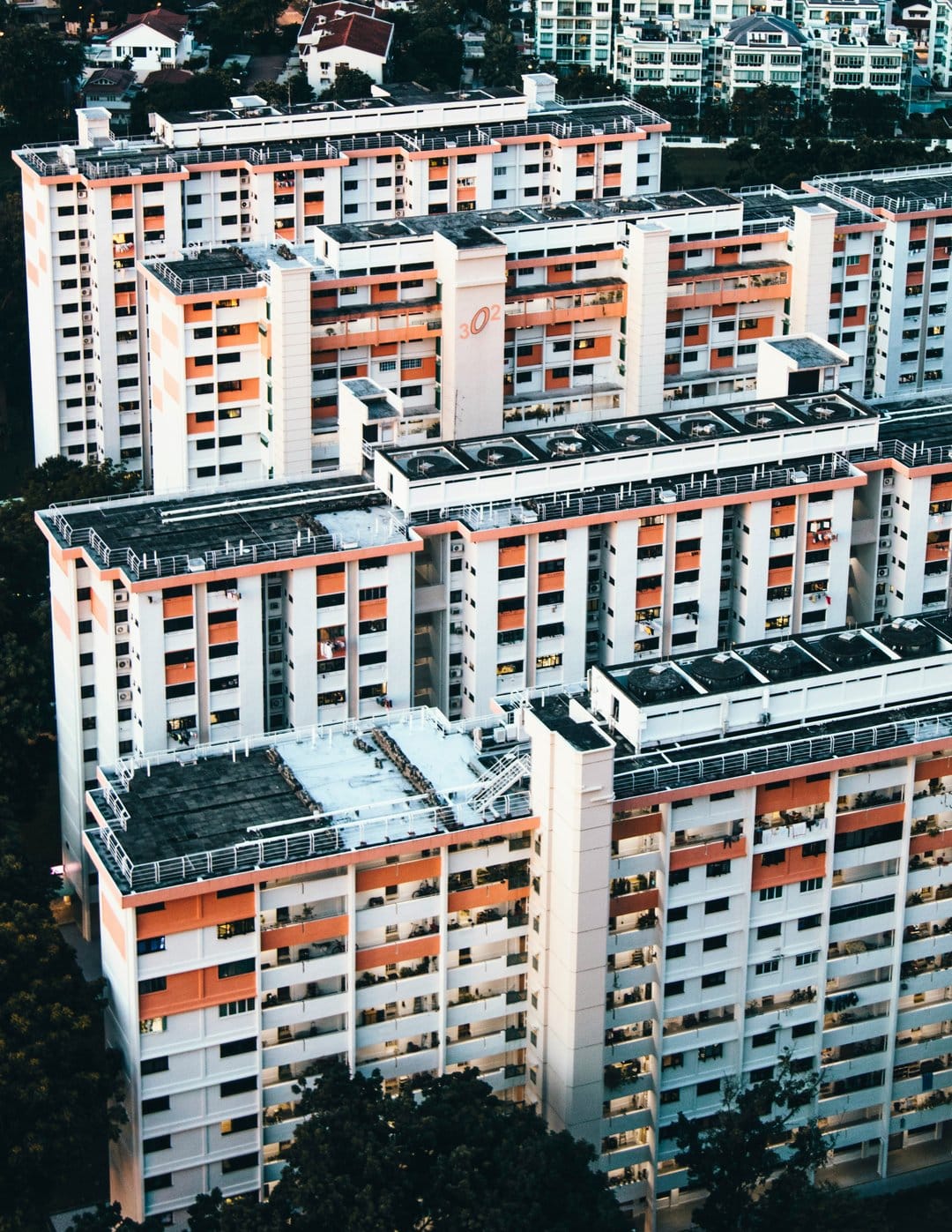 Singaporean apartment blocks with orange balconies and white walls surrounded by green trees from a drone view.
