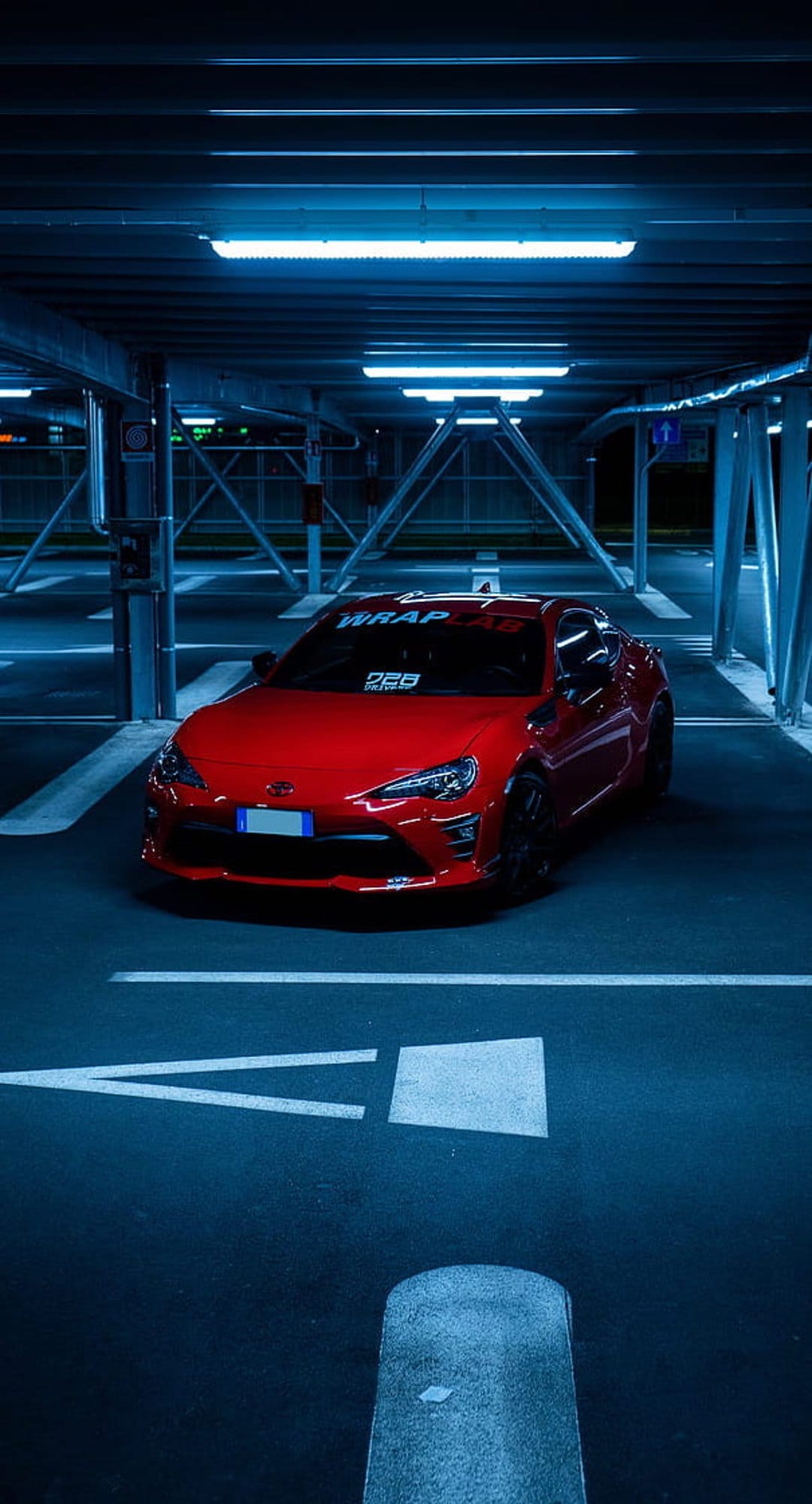 Red Toyota GT86 sports car parked in a blue-lit underground garage with white lines on the dark asphalt floor.