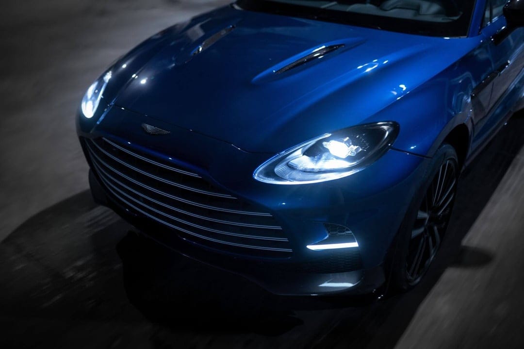 Metallic blue luxury SUV with illuminated LED headlights and sculpted hood vents in a dark setting.