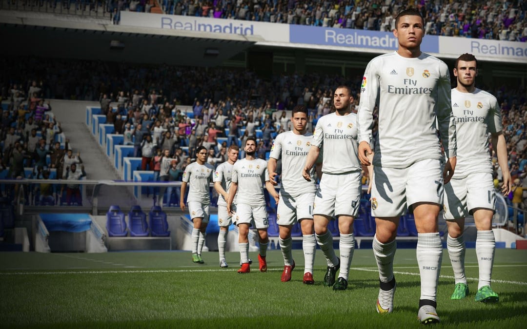 Cristiano Ronaldo leads the Real Madrid team onto a sunny green football pitch inside a crowded stadium.