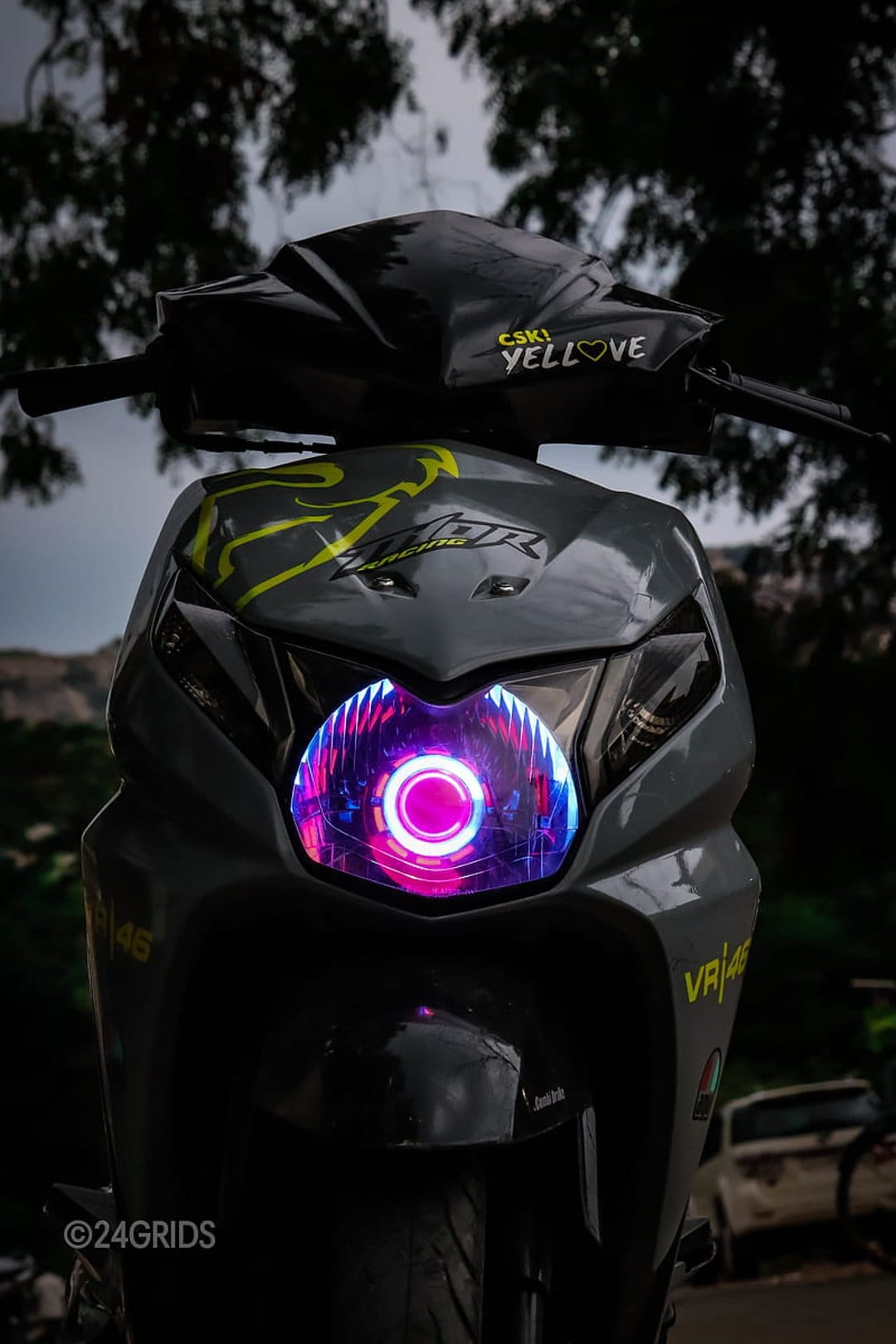 Honda Dio scooter featuring a glowing pink LED headlight and VR46 yellow graphics against a background of trees.