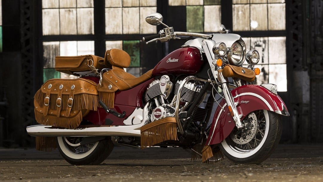 Maroon Indian Chief Vintage motorcycle with tan leather fringe and chrome accents in an industrial setting.