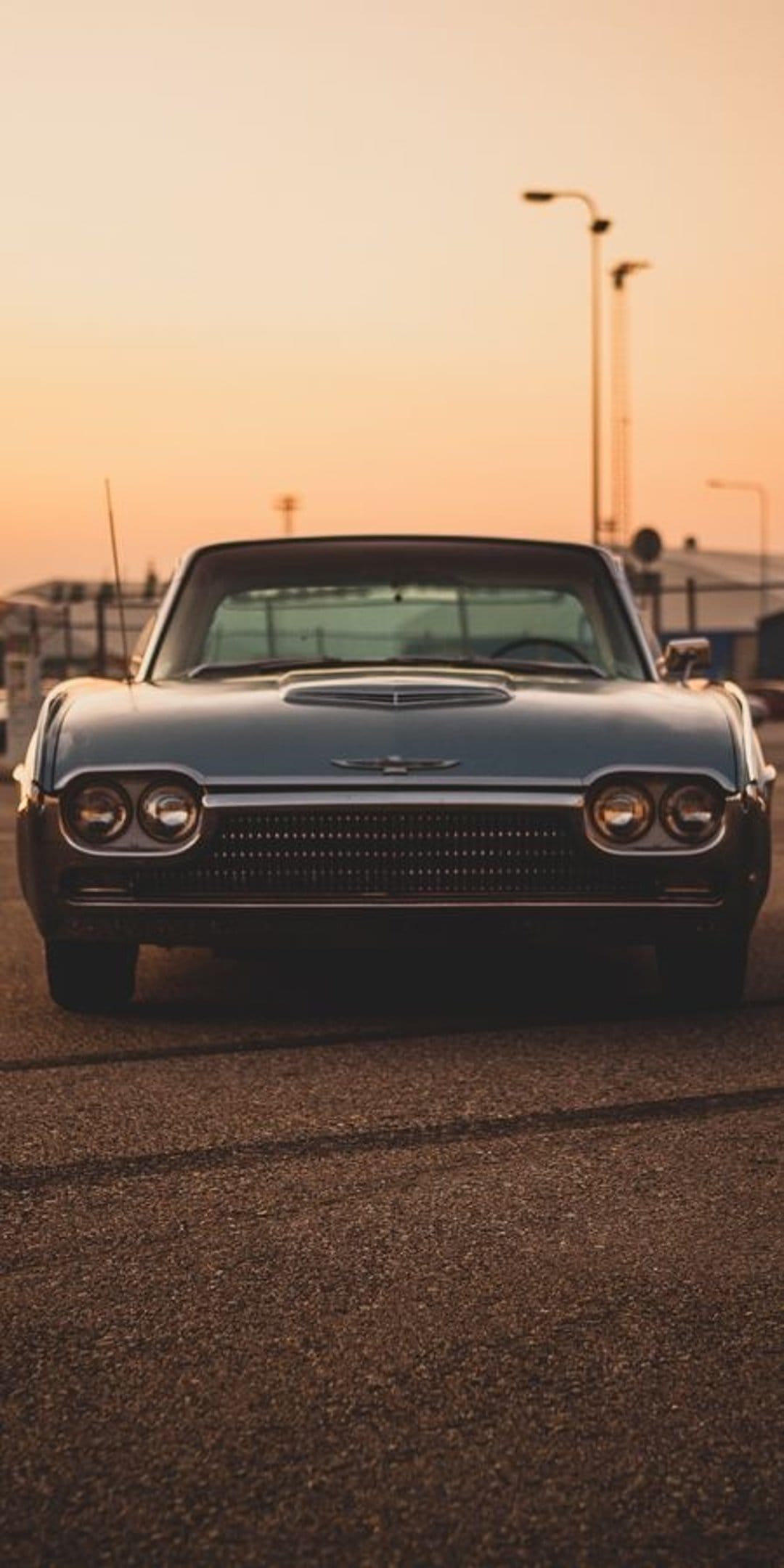 Dark blue Ford Thunderbird with round headlights parked on asphalt during a golden sunset with soft streetlights.