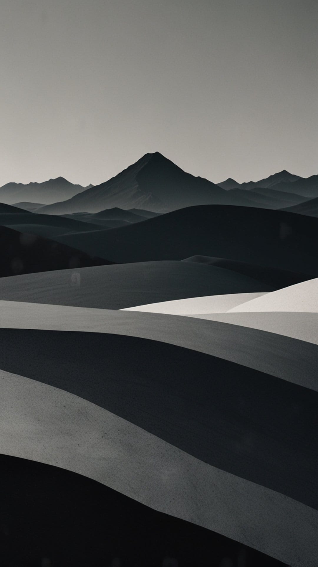 Sculpted sand dunes with deep shadows lead toward misty mountain peaks in a minimalist black and white landscape.