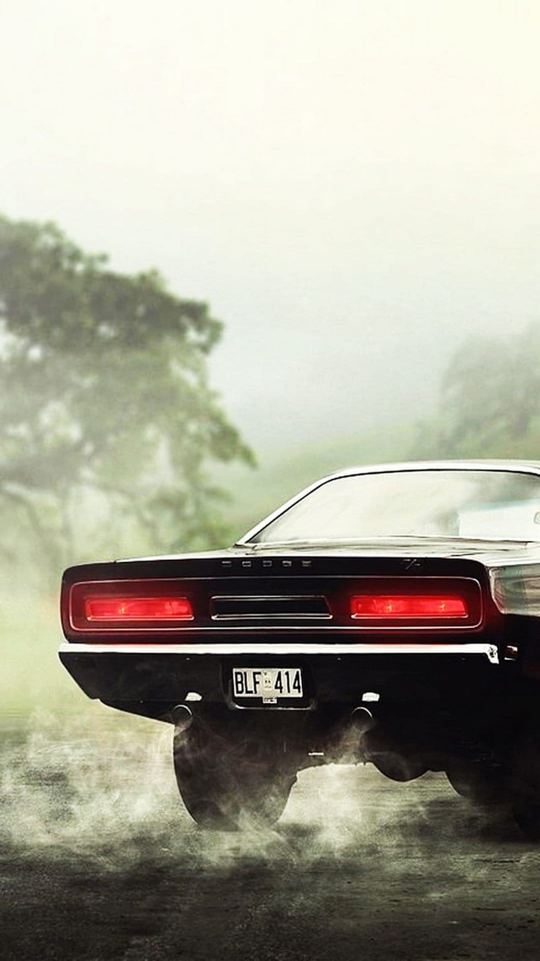Black Dodge Challenger rear view with glowing red taillights amidst grey smoke and fog in an outdoor setting.