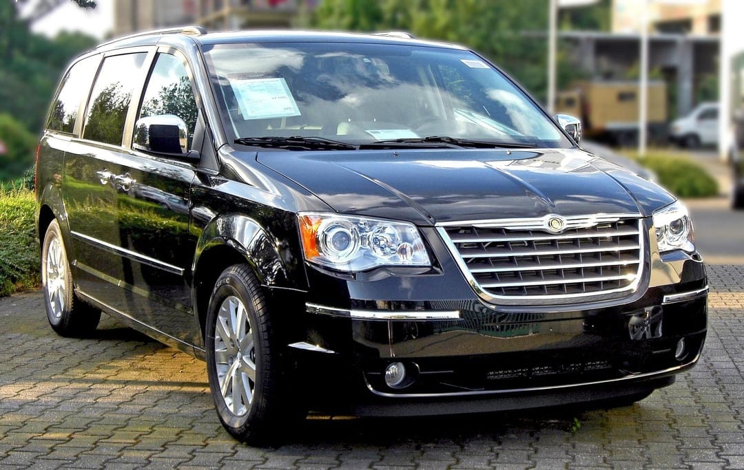 Front view of a black Chrysler minivan parked on textured gray bricks with a blurred green background.