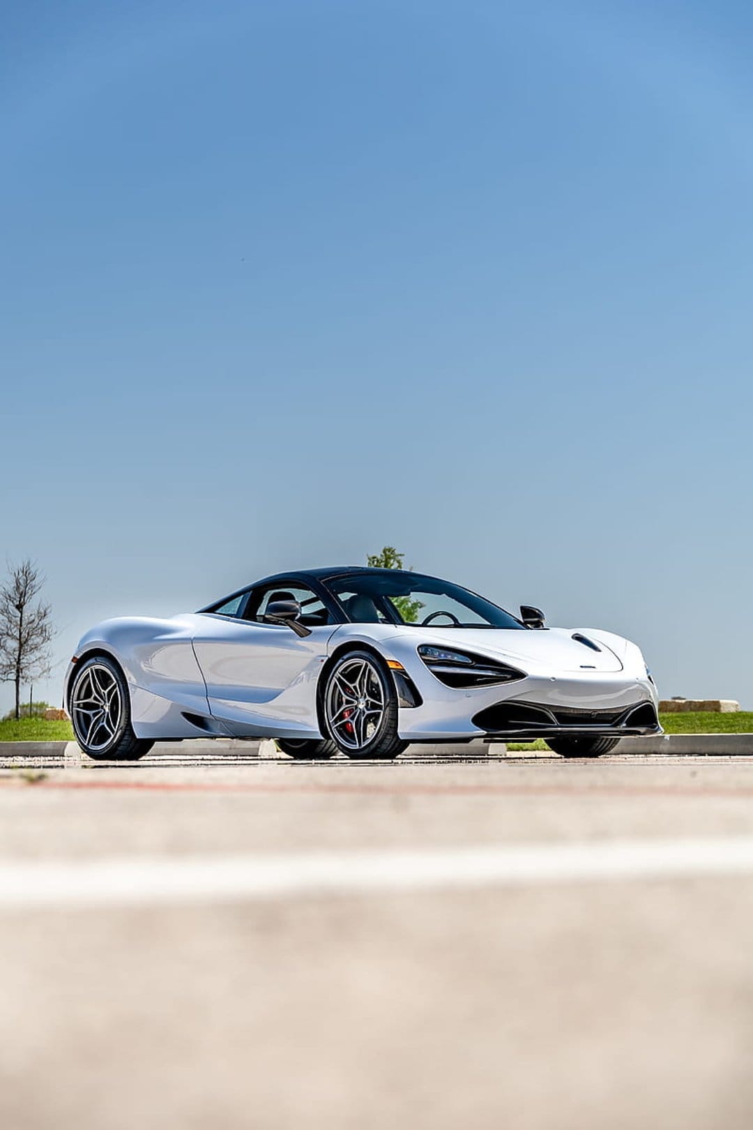 White McLaren 720S sports car with a black roof and alloy wheels parked outdoors under a bright blue sky.