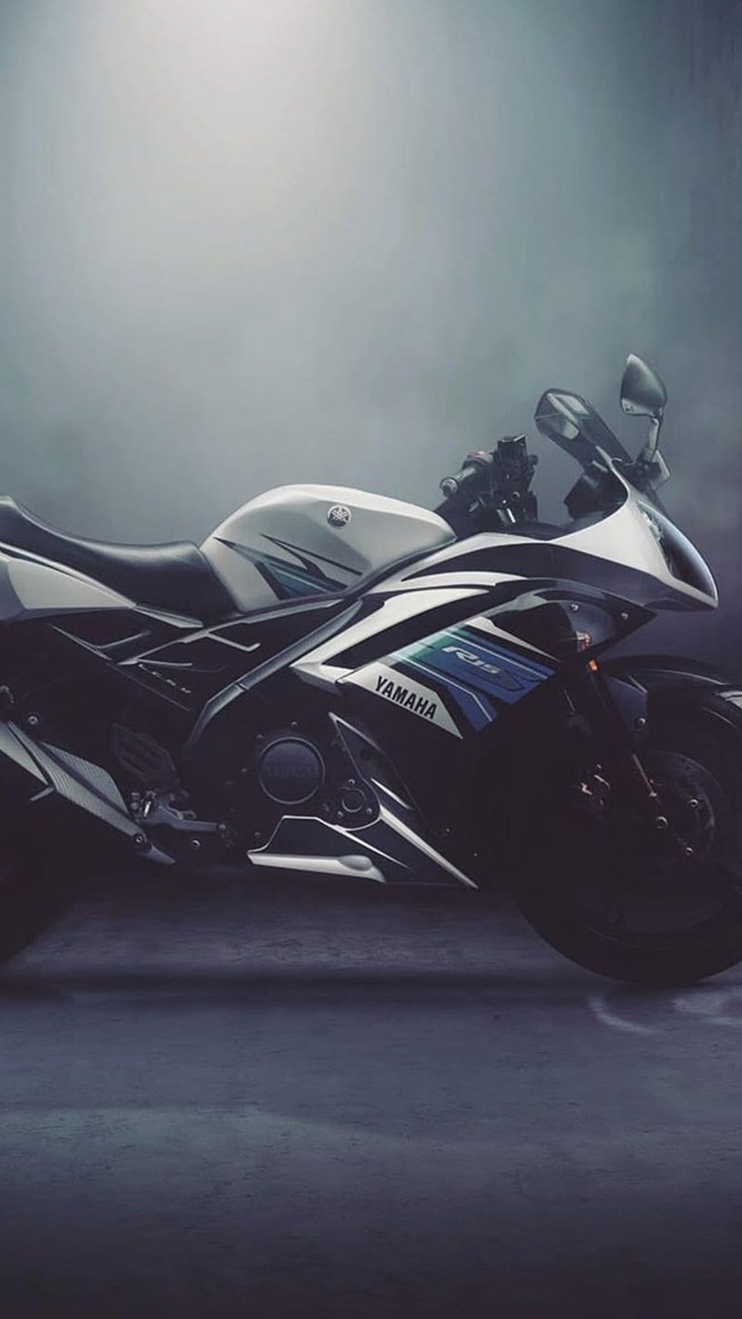 Yamaha R15 motorcycle with white fairings and blue accents parked on a dark textured surface with smoky background