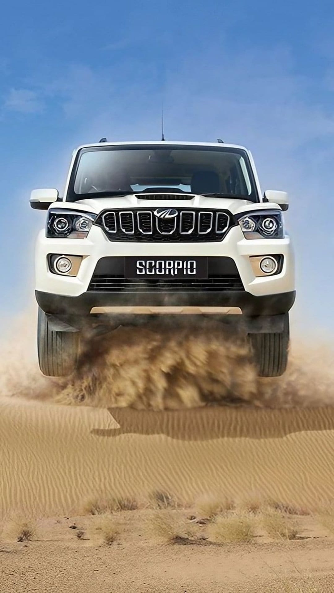 White Mahindra Scorpio SUV drifts through golden desert sand dunes under a clear blue sky creating a dust cloud.