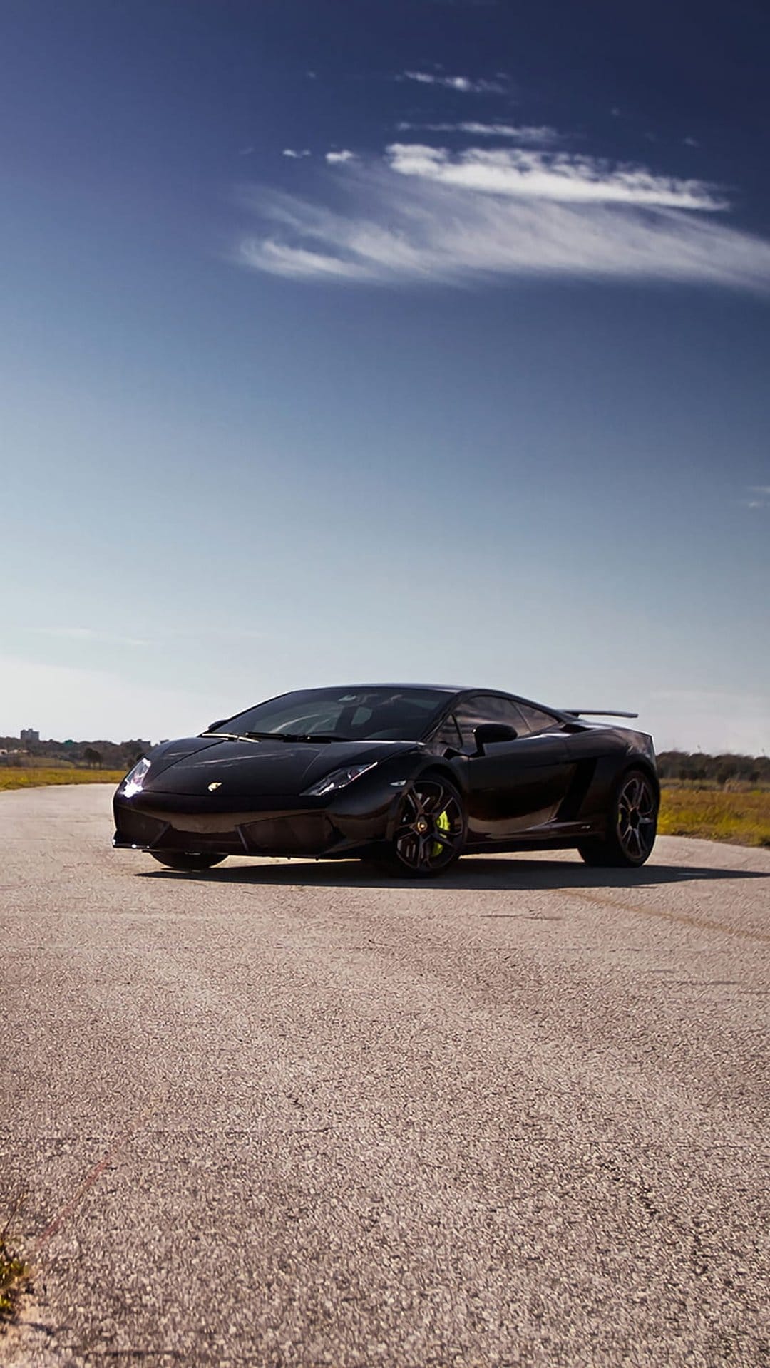 Black Lamborghini Gallardo with yellow brake calipers on a grey asphalt road under a bright blue sky.