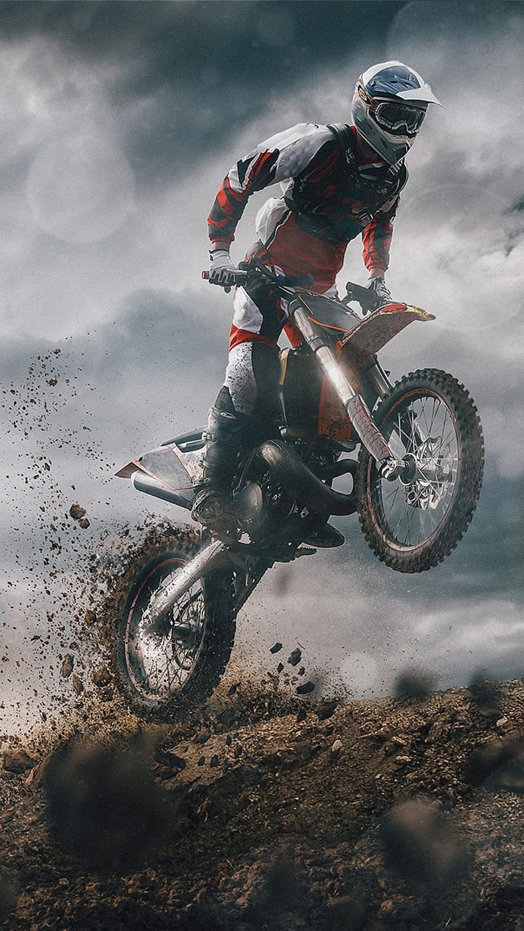 Motocross rider mid-air during a dirt bike jump with mud splashing below against a cloudy, dramatic sky.