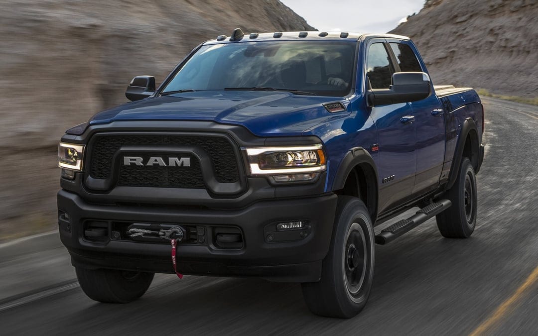 Blue RAM 2500 Power Wagon with a front winch driving on a winding road through rocky desert mountains.