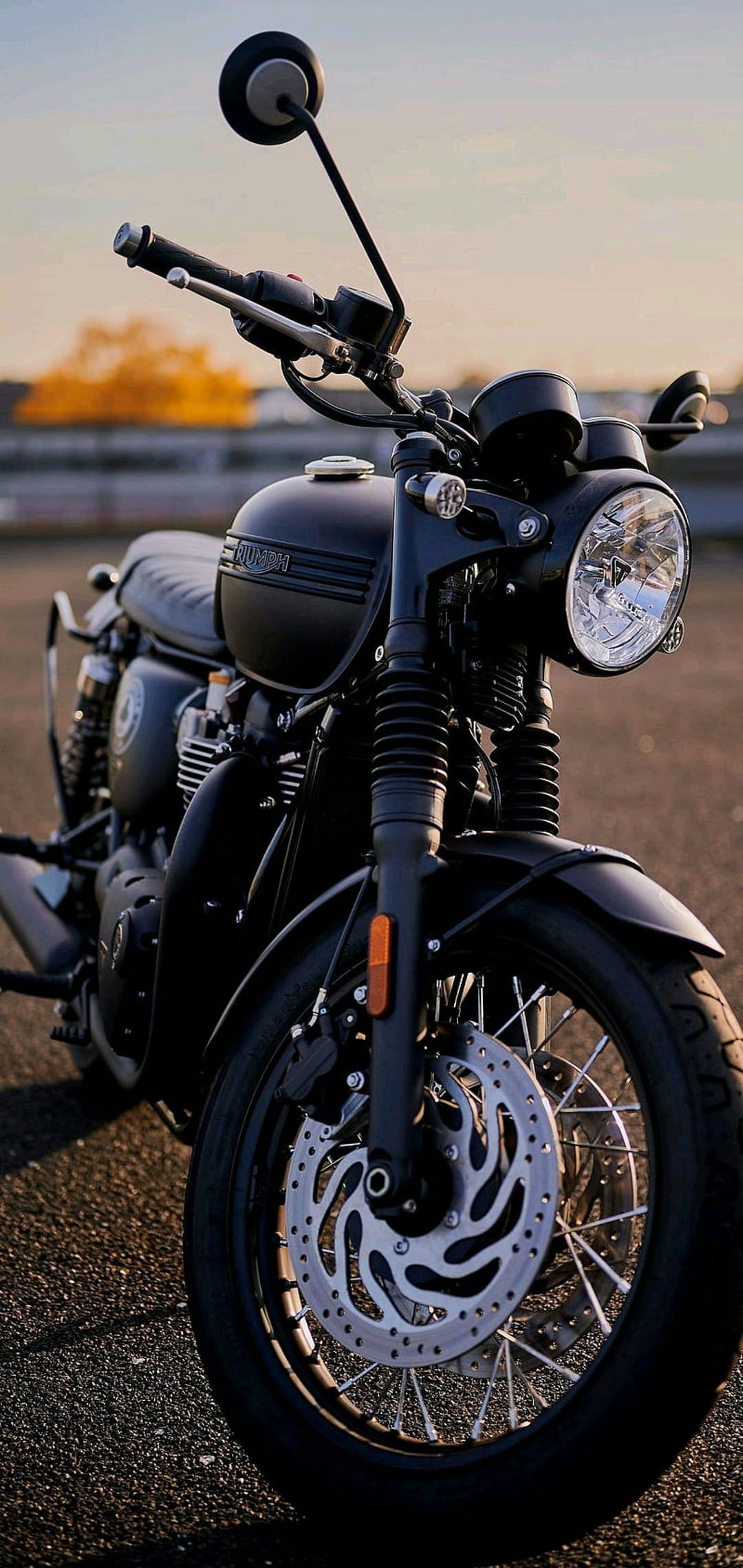 Black Triumph motorcycle with chrome accents parked on asphalt during golden hour with warm sunset reflections.