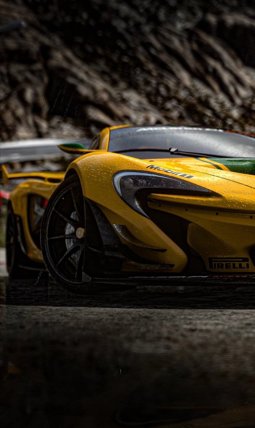 Yellow McLaren P1 supercar with glistening raindrops on its hood driving on a wet track near rocky terrain.