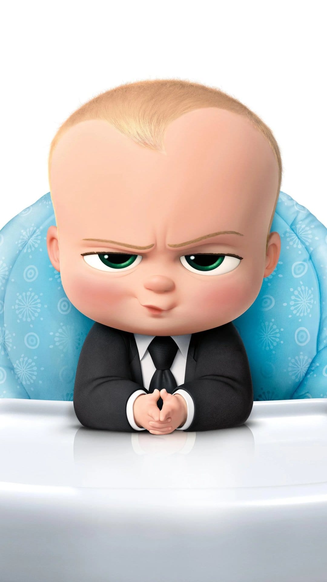 Boss Baby in a black suit with a stern, scheming face sits in a blue patterned high chair against a white wall.