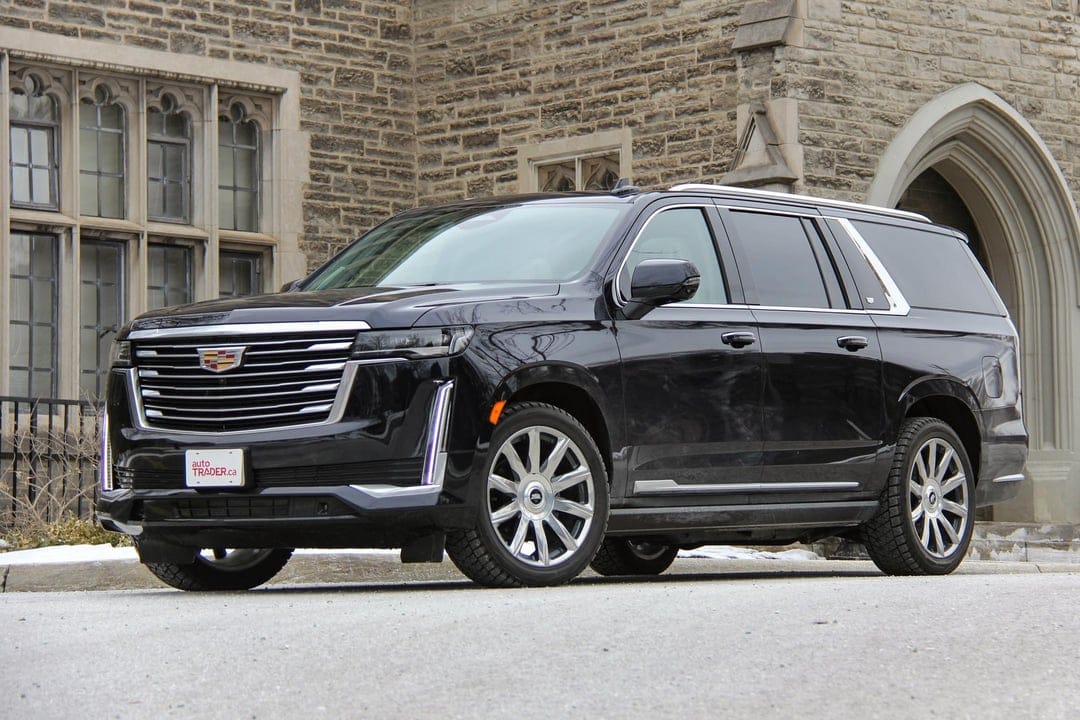 Black Cadillac Escalade luxury SUV parked on a street in front of a grand stone building with arched windows.