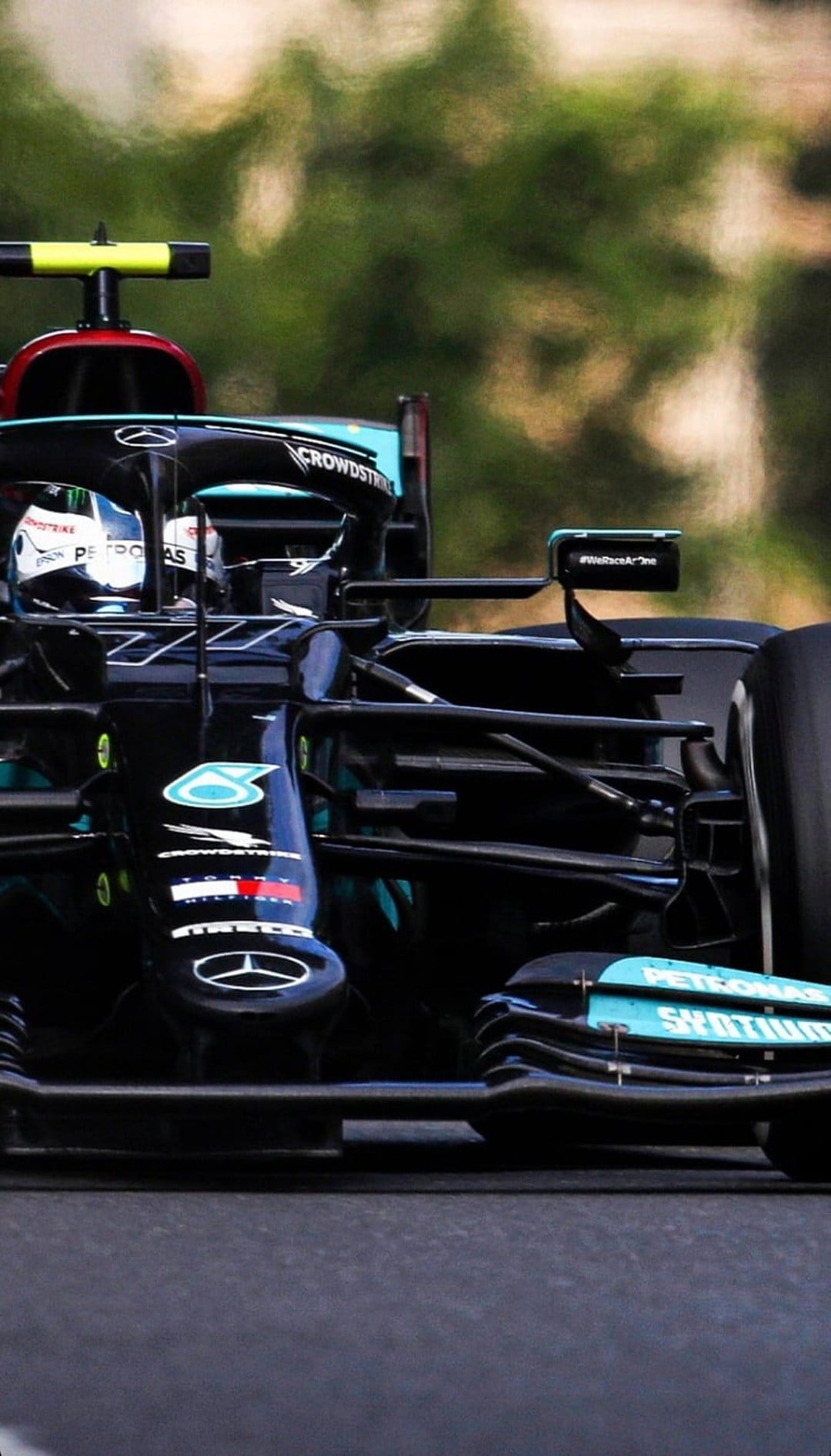 Mercedes Formula 1 car with Petronas branding races on a track against a backdrop of blurred green trees.