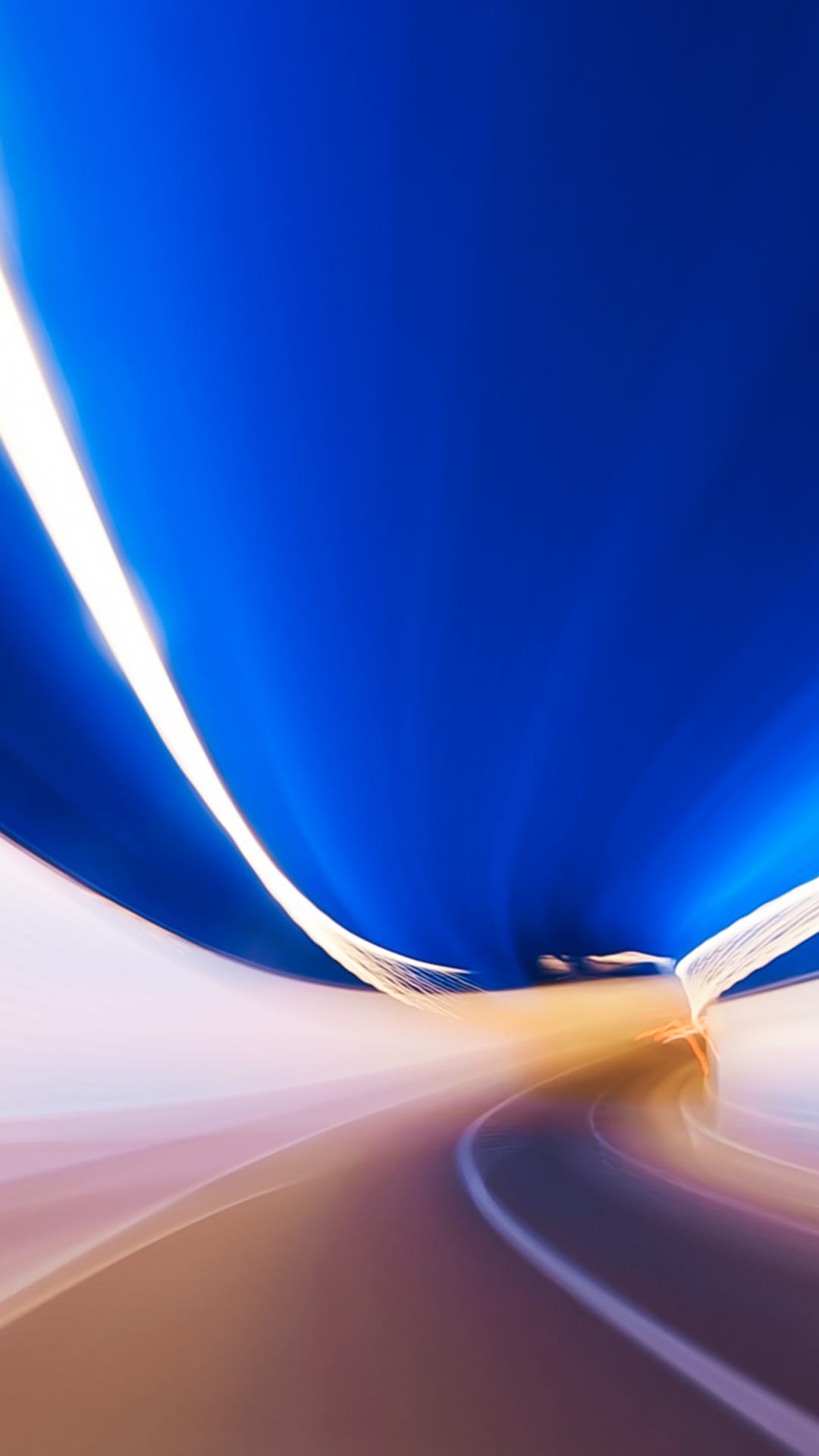 White and golden light trails curve sharply along a dark road under a deep blue sky with motion blur.