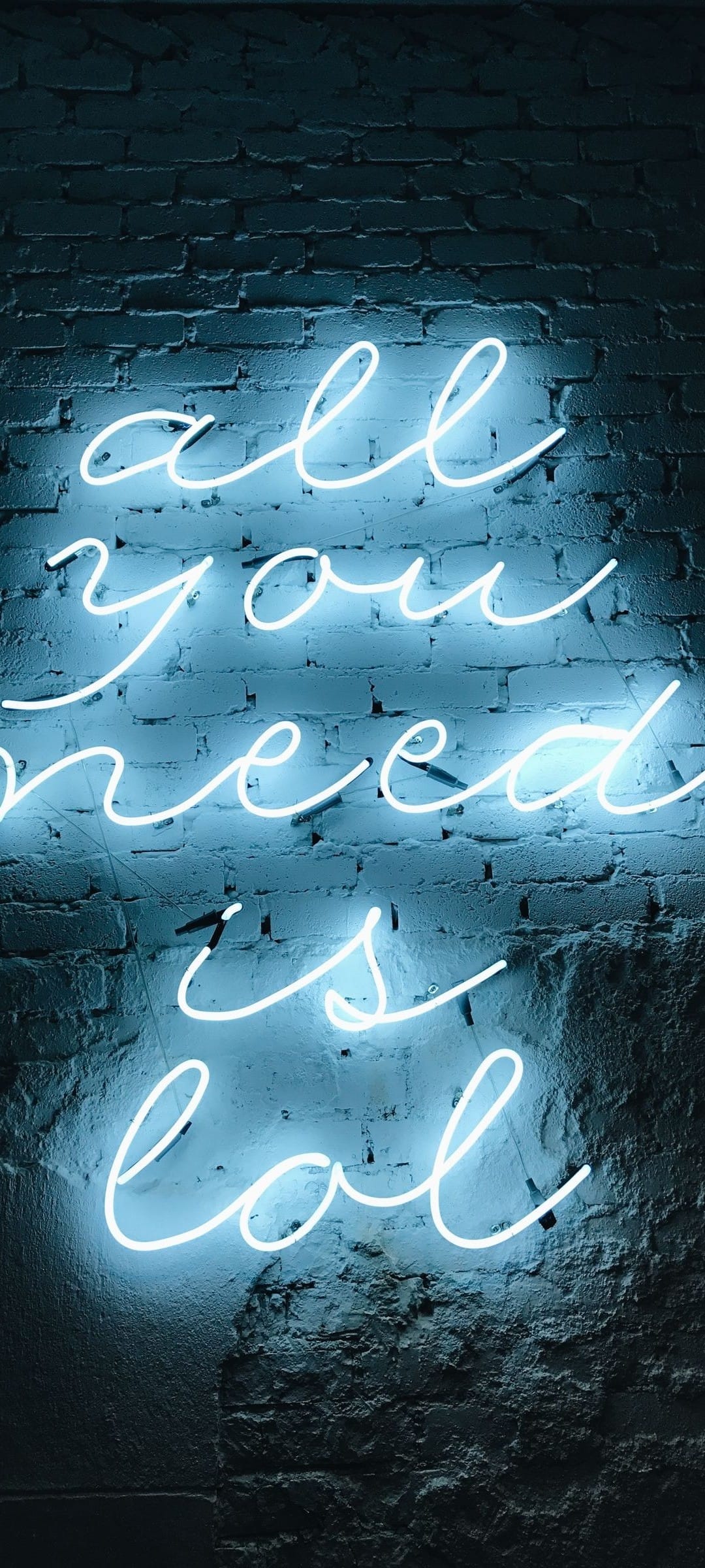 Blue neon cursive sign reading All You Need is Eat mounted on a dark textured brick background.