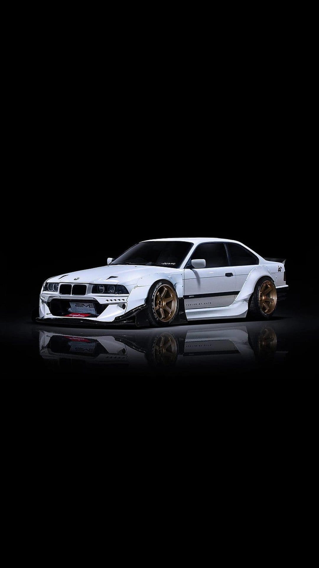 White BMW M3 E36 drift car with a widebody kit and bronze wheels parked against a solid black background.