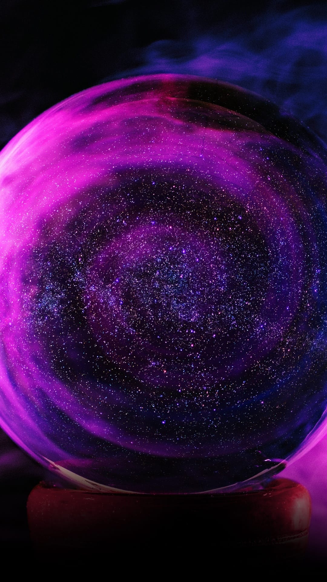 Glass orb containing a purple galaxy and stardust sits on a wooden base surrounded by wisps of white smoke.