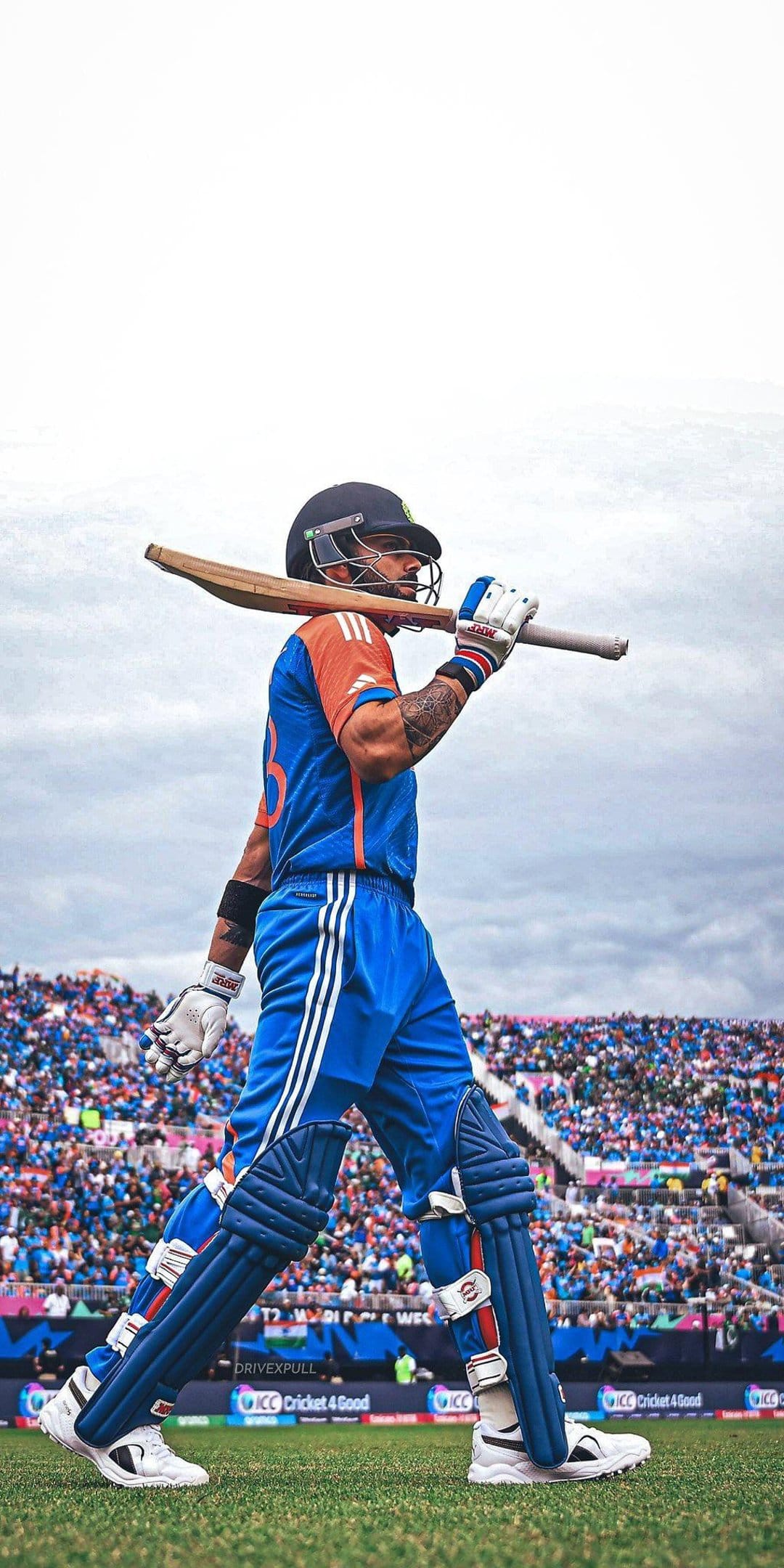 Virat Kohli walks off a cricket field carrying a bat over his shoulder while wearing a blue jersey and helmet.