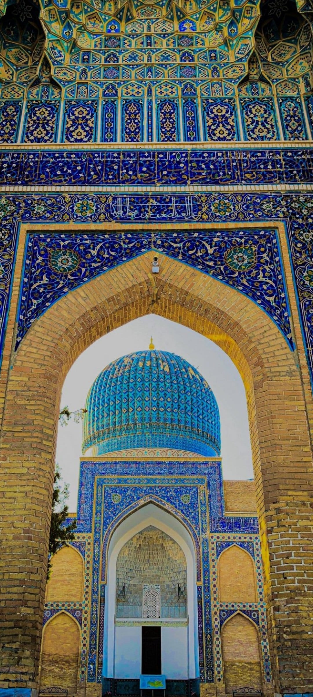 Blue tiled dome and arched entrance of a mosque featuring intricate geometric mosaics and Arabic calligraphy.