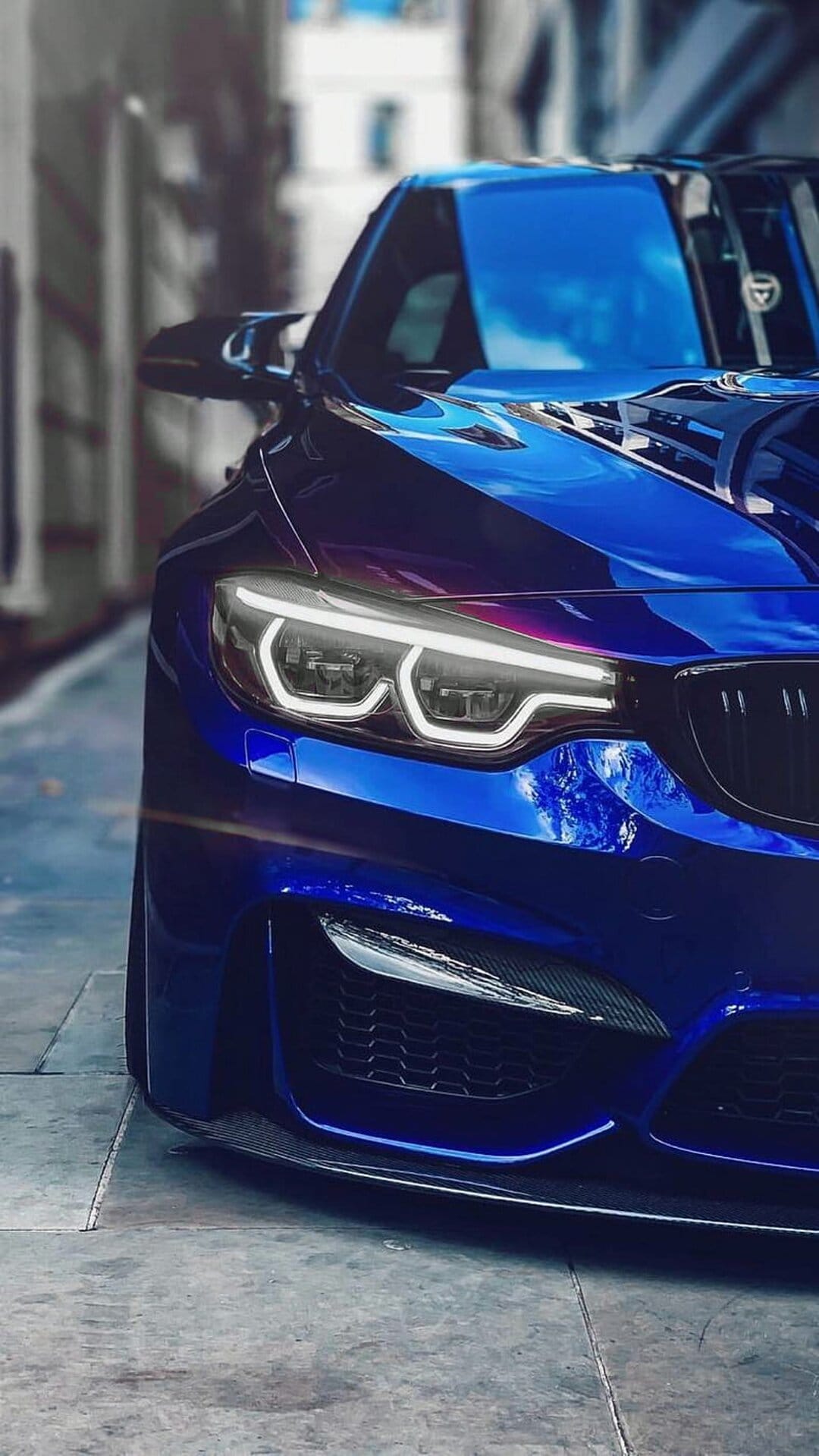 BMW M4 front end featuring blue metallic paint, glowing LED headlights, and a black kidney grille in close-up.