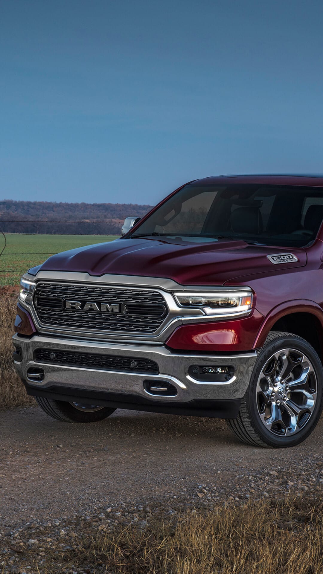 Maroon Ram 1500 truck with a polished chrome grille and LED headlights on a gravel path under a clear blue sky.