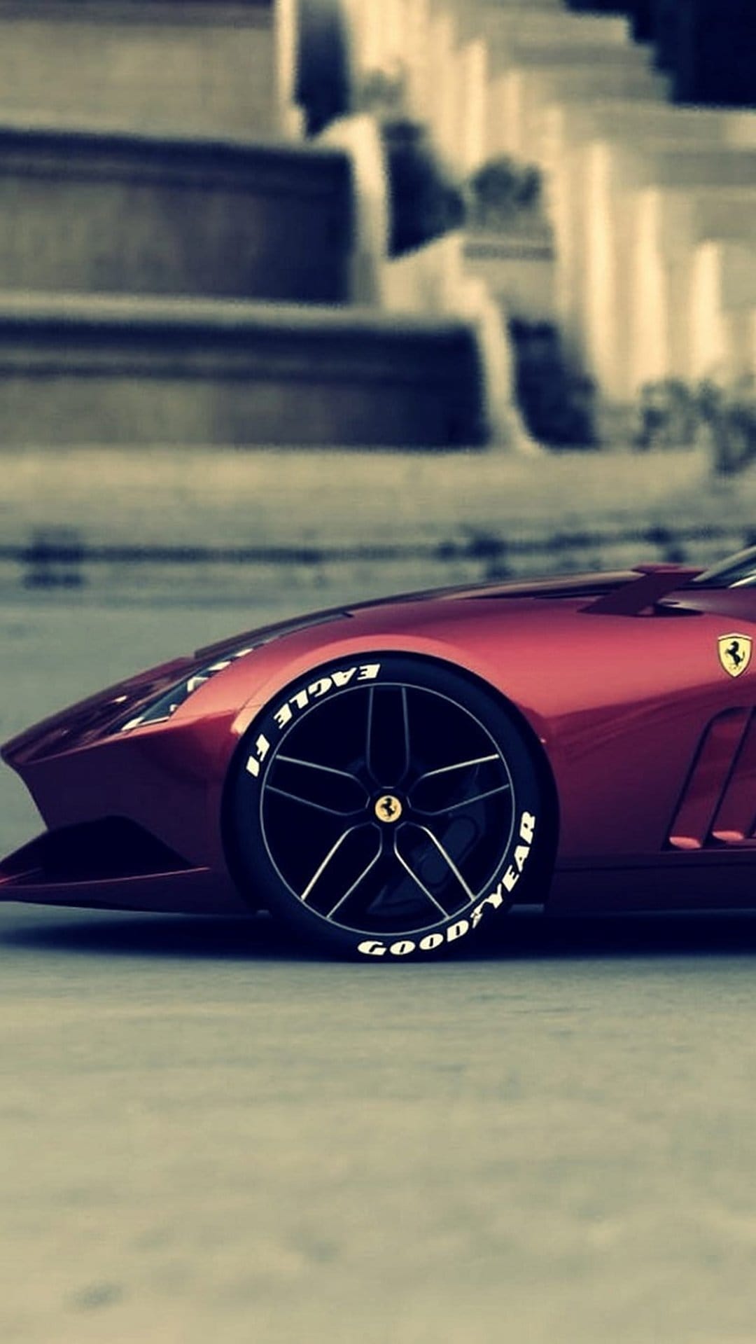 Crimson Ferrari wheel and Goodyear Eagle F1 tire positioned against a background of blurred stone steps.