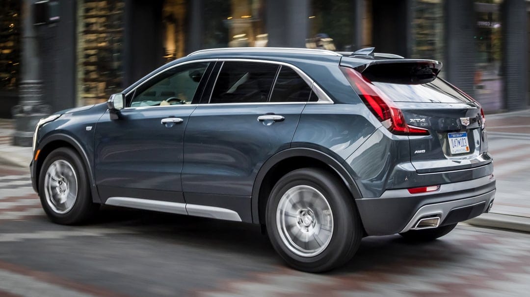 Cadillac XT4 luxury SUV driving on a city street with motion blur on wheels and blurred urban background.